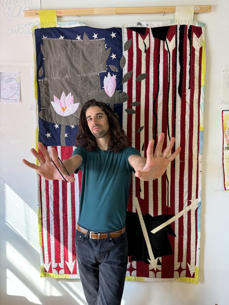 Alex Kalil standing palms-out in front of a quilted American flag with lotus flowers.